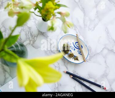 Colpo ad angolo alto di una marijuana smussata e pezzi di cannabis secca con fiori sfocati nei vasi Foto Stock