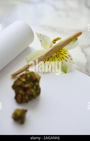 Colpo di closeup verticale di un pezzo di cannabis secca e. una smussatura su una carta bianca Foto Stock