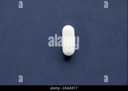 Primo piano di una singola pillola bianca su un bianco surface - il concetto di dipendenza Foto Stock