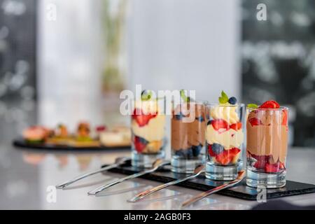 Primo piano di deliziosi dolci alla frutta e al cioccolato in vetro tazze su un vassoio nero Foto Stock