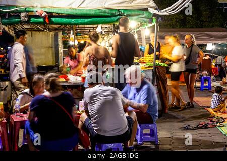 I turisti seduti a un cibo di strada in stallo a Phnom Penh il Mercato Notturno, Phnom Penh Cambogia. Foto Stock