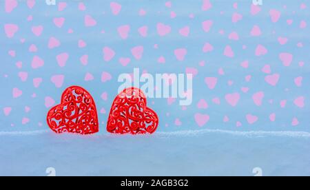 Il giorno di San Valentino Valentine card con due red openwork cuori in un cumulo di neve su uno sfondo blu con cuori rosa con sfondo spazio Foto Stock