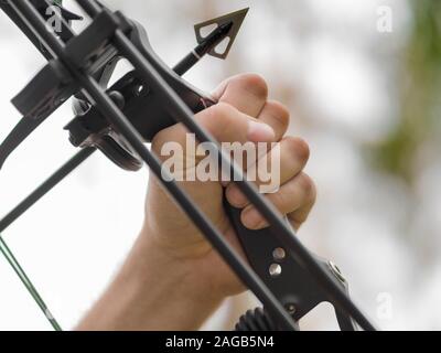 Archetto a caccia nella foresta. Close-up mano che impugna un arco moderno e un forte arrowhead. Foto Stock