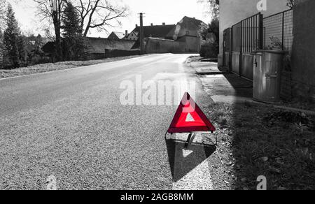 Attenzione! Pericolo sulla strada. Triangolo. Cartello stradale sul bianco e nero lo sfondo del villaggio. Simbolo di attenzione sul manto di asfalto. Regole del traffico. Foto Stock