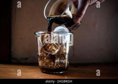 Colpo di closeup di una mano umana versando liquore in un vaso pieno di ghiaccio con sfondo sfocato Foto Stock