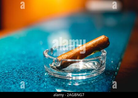 Colpo di primo piano di un sigaro in un posacenere su un tavolo con un abbigliamento da tavolo blu Foto Stock