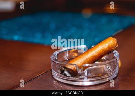 Colpo di primo piano di un sigaro in un posacenere su un tavolo con un abbigliamento da tavolo blu Foto Stock