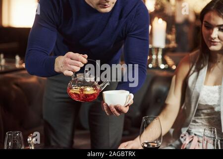 L'uomo analizzato il tè in tazza bianca. Amici di Famiglia con bel tempo in bella il lusso moderno ristorante Foto Stock