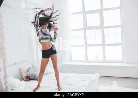 Ballando sul letto bianco. Brunette divertirsi sul loro tempo di fine settimana Foto Stock