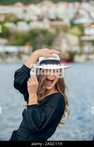 Elegante Attraente Pretty girl holding retrò hat, sorridente e posa per la migliore qualità di immagine. Vestiti alla moda felice donna romantica in ama camminare al Foto Stock