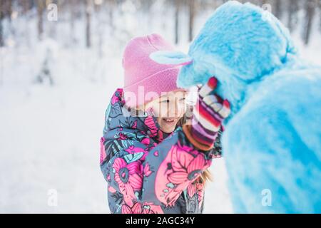 Primo piano di una ragazza felice che stringe le guance di una donna in un costume blu soffici Foto Stock