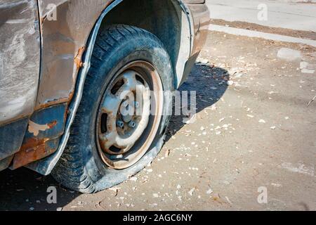 Close-up pneumatico danneggiato. La ruota del pneumatico auto perdita. Il pneumatico sgonfio in attesa per la riparazione. Abbandonato auto nel parcheggio. Foto Stock