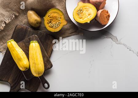 Vista superiore del taglio di legno pannelli con zucchine, patate, zucca e la piastra con il filato sulla superficie di marmo con hessian Foto Stock