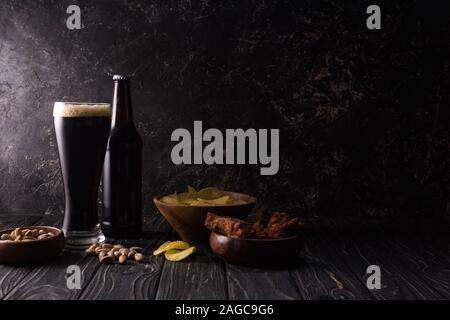 Vetro e bottiglia di birra vicino a bocce con i dadi, le patatine e le ali di pollo su un tavolo di legno Foto Stock