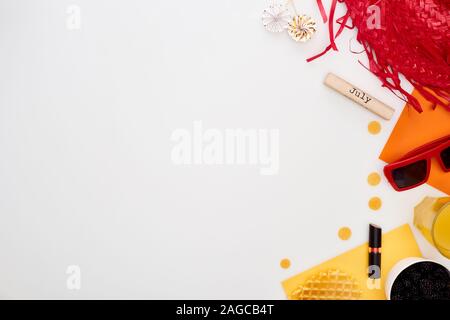 Blocco di legno con luglio iscrizione, occhiali da sole, lecca-lecca, occhiali da sole, succo di arancia, cappello di paglia, cialde, cosmetici isolato su bianco Foto Stock