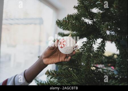 Primo piano immagine della ragazza di colore bianco di contenimento holiday ninnolo rosso con il simbolo del fiocco di neve su di esso appeso su albero di Natale. Foto Stock