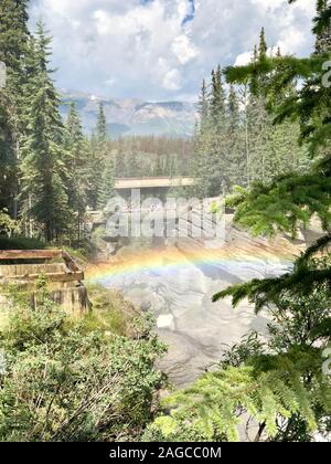 L'arcobaleno sulle formazioni rocciose circondato da abeti verdi alberi sotto il cielo nuvoloso Foto Stock