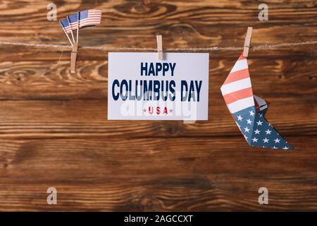 Scheda con happy Columbus day iscrizione tra American bandiere nazionali e la barca di carta su una superficie di legno Foto Stock