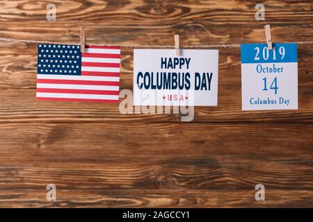 Scheda con happy Columbus day iscrizione nelle vicinanze American bandiera nazionale e calendario foglio di carta con 14 ottobre data su una superficie di legno Foto Stock