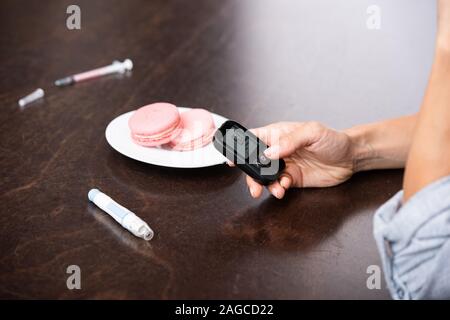 Vista ritagliata della donna che mantiene il monitoraggio di glucosio nei pressi di dessert Foto Stock
