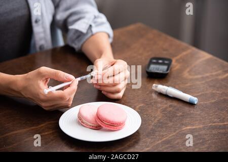 Vista ritagliata della donna tenendo la siringa vicino a dessert e bisturi Foto Stock