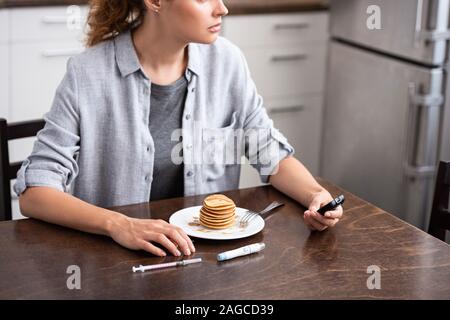 Vista ritagliata della donna con diabete Tenendo il glucosio monitor vicino pancake Foto Stock