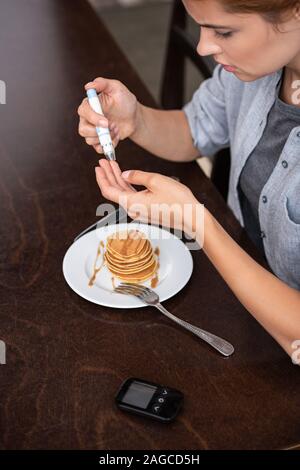 Donna con il diabete facendo prova di sangue con sangue lacet vicino a pancake Foto Stock