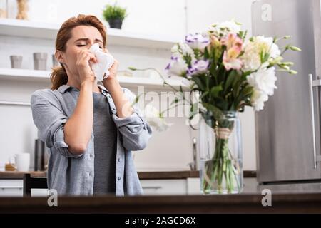 Messa a fuoco selettiva di donna con allergia da polline starnuti nel tessuto vicino a fiori Foto Stock