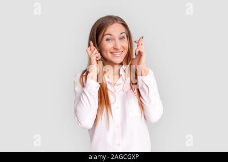 Freestyle. Giovane donna in piedi isolato su bianco dita incrociate sorridente sperando per una migliore Foto Stock
