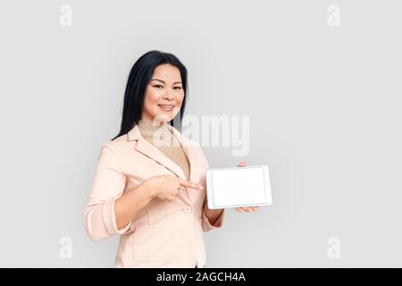 Freestyle. Imprenditrice asiatici in piedi isolato su bianco rivolto a schermo della tavoletta digitale sorridente fiducioso lo spazio di copia Foto Stock