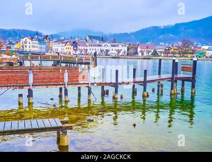 A piedi lungo argine del lago Traun (Traunsee) con vista sul molo vecchio e nebbiosa città vecchia di Gmunden sullo sfondo, Austria Foto Stock