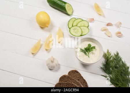 Salsa Tzatziki nella ciotola con gli ingredienti più freschi e pane bianco su sfondo di legno Foto Stock