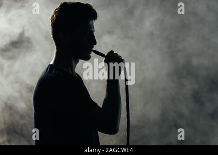 Silhouette di uomo di fumare narghilè in fumo nelle tenebre Foto Stock