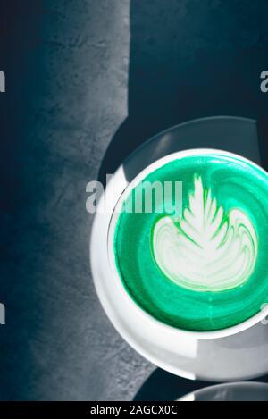 Tazza di Verde matcha latte nel caffè, bella giornata di sole, ombre sul tavolo Foto Stock