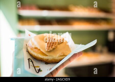 Persona che tiene una ciambella deliziosa con un tovagliolo su un sfondo sfocato Foto Stock