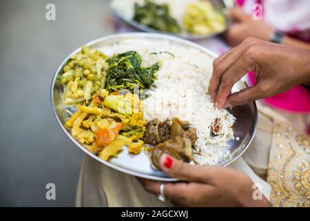 Donna indiana che mangia piatti tradizionali con riso, piselli, carne e verdure in un vassoio d'argento Foto Stock