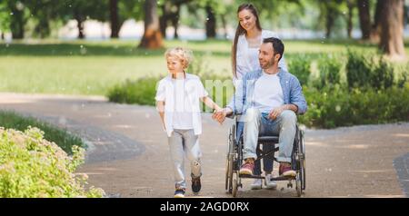 Panoramica della madre bella sedia a rotelle di rotolamento con padre disabili nel parco vicino figlio Foto Stock