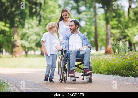 Madre bella sedia a rotelle di rotolamento con padre disabili nel parco vicino figlio Foto Stock