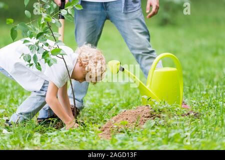 Figlio di piantare la piantina nel terreno in prossimità di padre in posizione di parcheggio Foto Stock