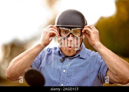 Uomo seduto su una motocicletta che indossa gli occhiali di equitazione e facendo un divertente volto. Foto Stock
