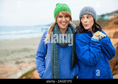 Due giovani donne che indossano un abbigliamento caldo mentre in spiaggia in inverno. Foto Stock