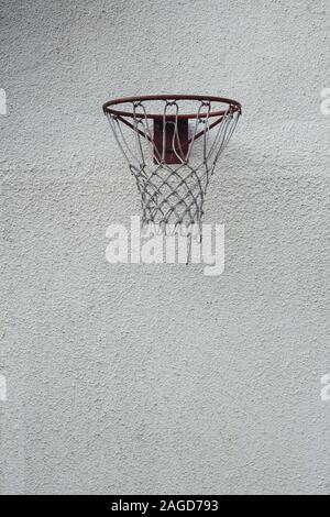 Immagine verticale di un cerchio rosso da basket su un sporco parete bianca durante il giorno Foto Stock