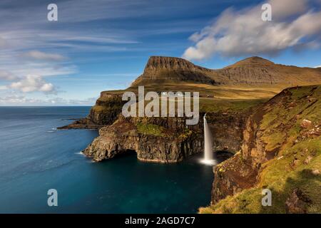 Villaggio Gasadalur e sorprendente cascata Mulafossur con rainbow al di sopra del Nord Oceano Atlantico. Le isole Faerøer. La Danimarca. Lunga esposizione. Foto panoramica per Foto Stock