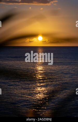 Immagine verticale affascinante del sole che si tramonta dietro le nuvole sopra l'oceano calmo Foto Stock