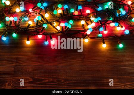 Bordo di Natale con colorati garland. Natale sfondo scuro sulla scrivania in legno. Appartamento laico, vista dall'alto, copia dello spazio. Foto Stock