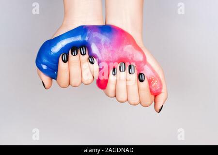 Mani con manicure nero tenendo il fango in blu e rosa colori vibranti Foto Stock
