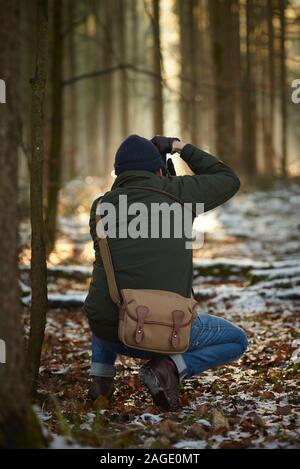 Fotografo che scatta foto in una foresta circondata da vegetazione coperta con neve e foglie Foto Stock