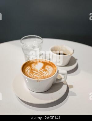 Colpo verticale di un tavolino con una tazza di cappuccino, un bicchiere d'acqua e caffè a metà bendata Foto Stock