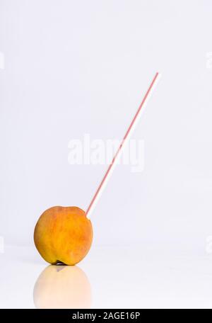 Colpo verticale di una paglia di succo in una pesca riflettente su sfondo bianco Foto Stock