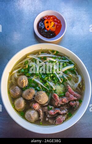 Foto verticale di carni cotte Pho vietnamita ciotola e di salsa al peperoncino Foto Stock